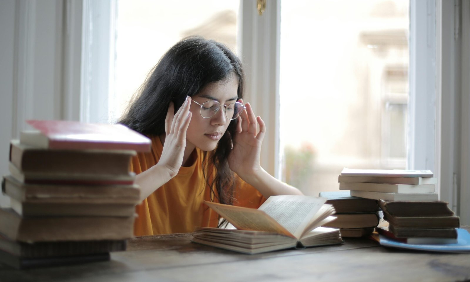 Girl wearing glasses looking overwhelmed and fatigued while surrounded by books, illustrating the struggle of staying energized during intense study sessions